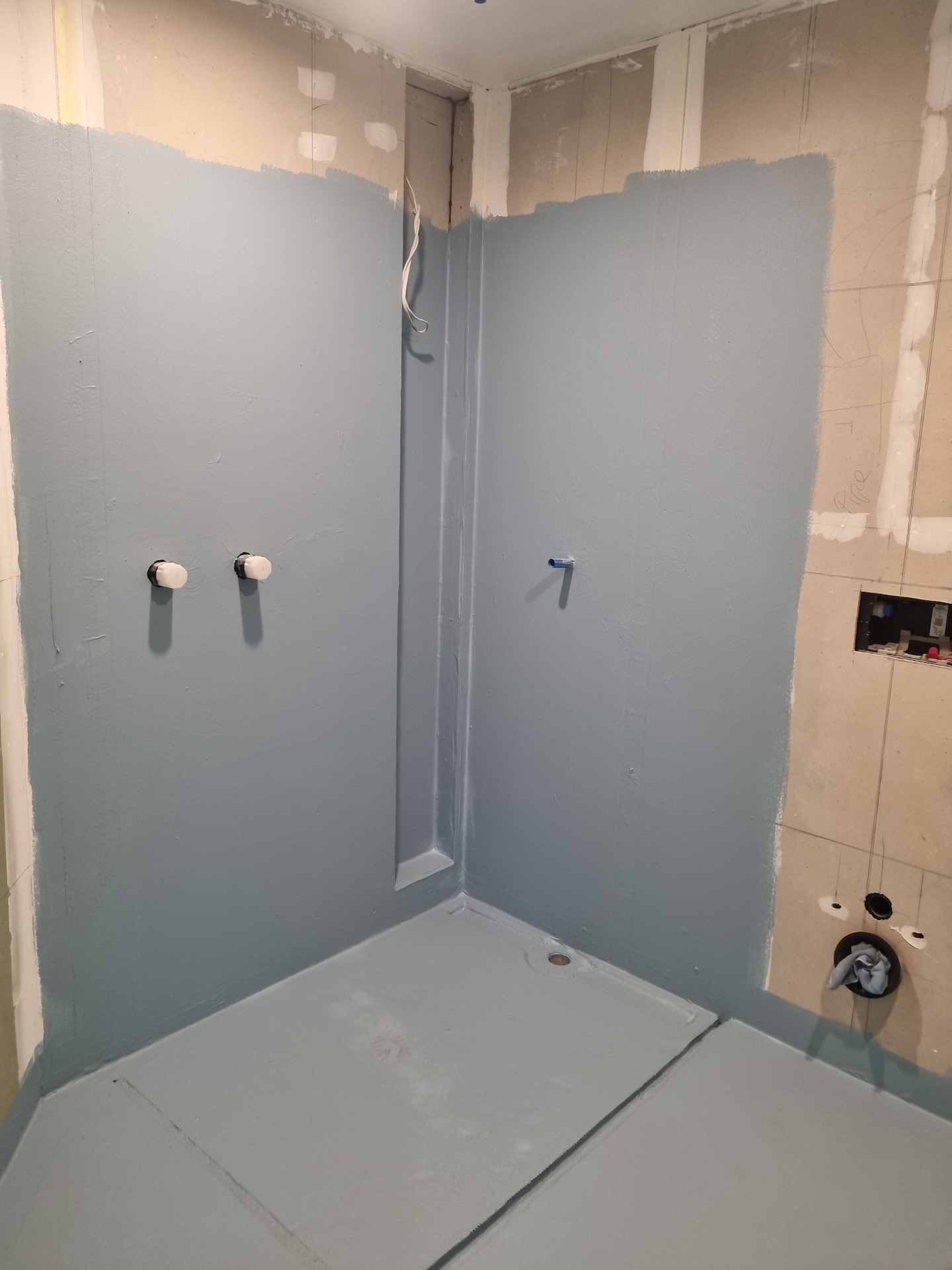 Bathroom renovation in Auckland, New Zealand, showing the crucial stage of waterproofing the shower area with a blue membrane applied to the walls and floor, ensuring protection against water damage before tiling.