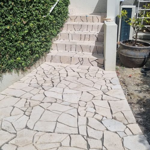 Newly installed stone paving leading up a set of stairs, featuring irregular-shaped coloured flagstones creating a mosaic-like pathway.
